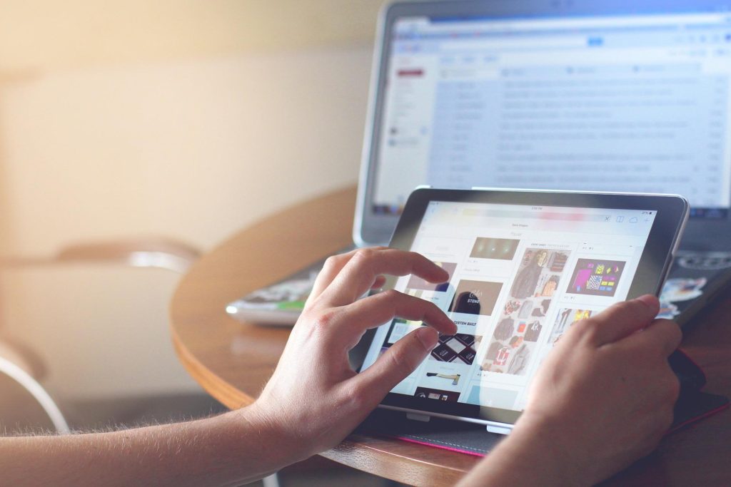 hands touching touchscreen tablet with laptop screen in background