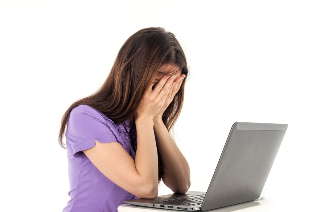 woman covering face at laptop